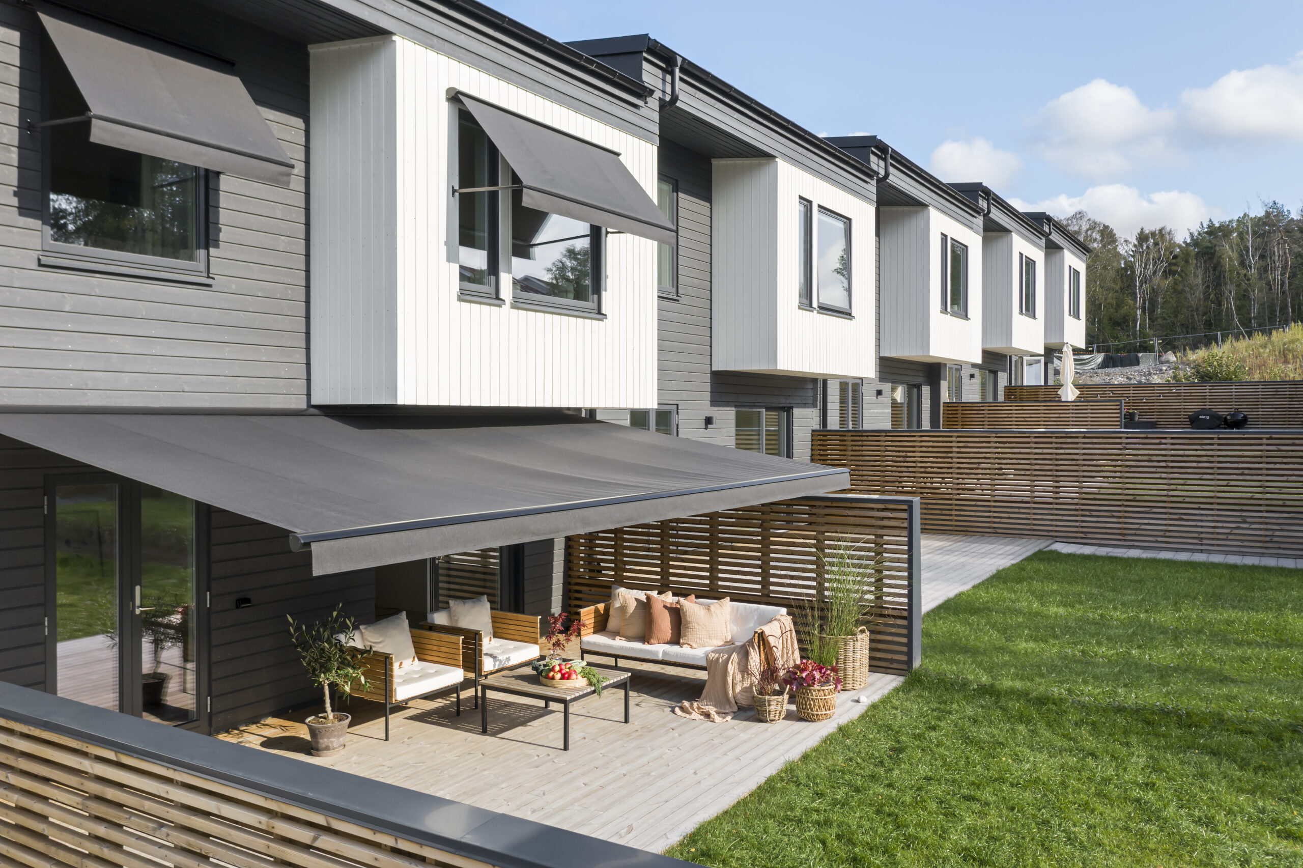 Gråa fönstermarkiser och terrassmarkis på radhus.