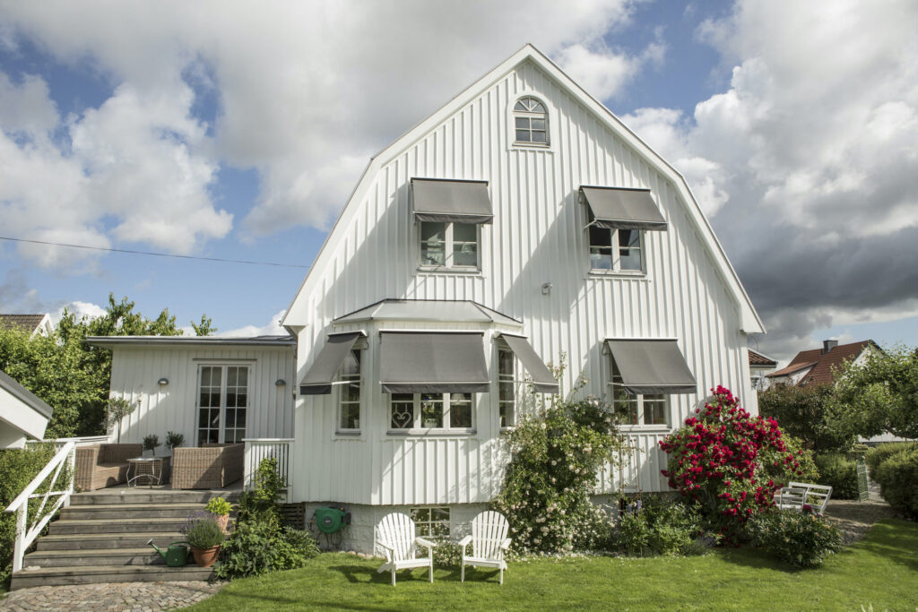 Gråa fönstermarkiser på vit villa.