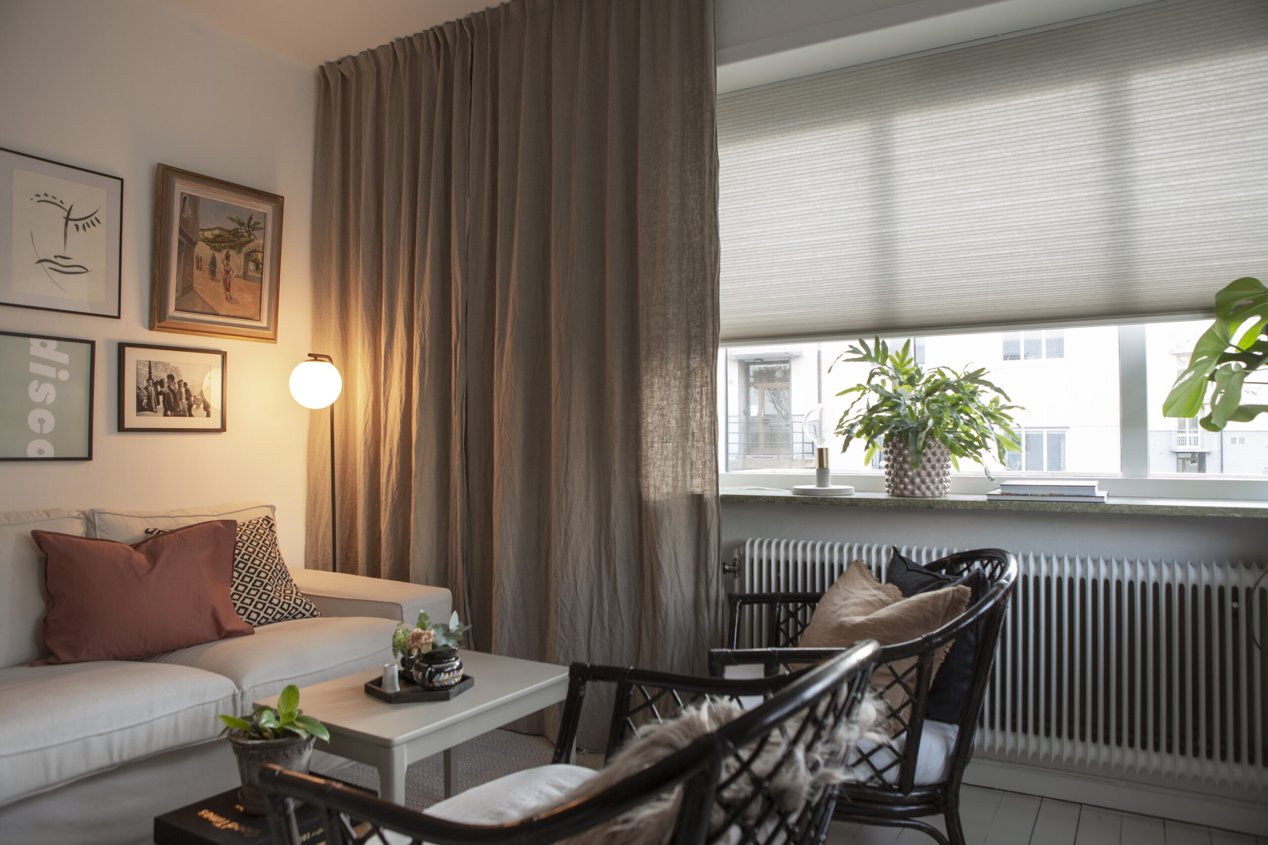 Beige duettegardin i gardinskenor bakom gardin i vardagsrum.