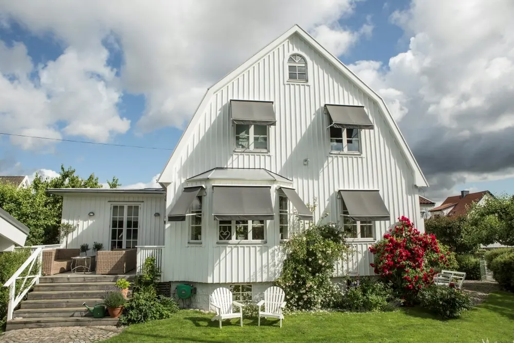 Gråa fönstermarkiser på vit villa.