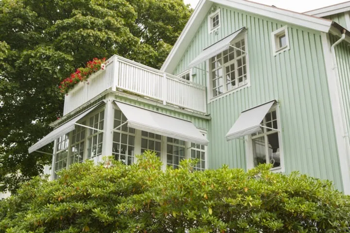 Gråa fönstermarkiser på grön villa.